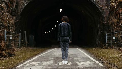 Rückansicht einer Frau, die mitten auf der Straße vor einem Tunnel steht.