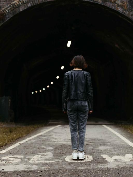 Rückansicht einer Frau, die mitten auf der Straße vor einem Tunnel steht. Rückansicht einer Frau, die mitten auf der Straße vor einem Tunnel steht.