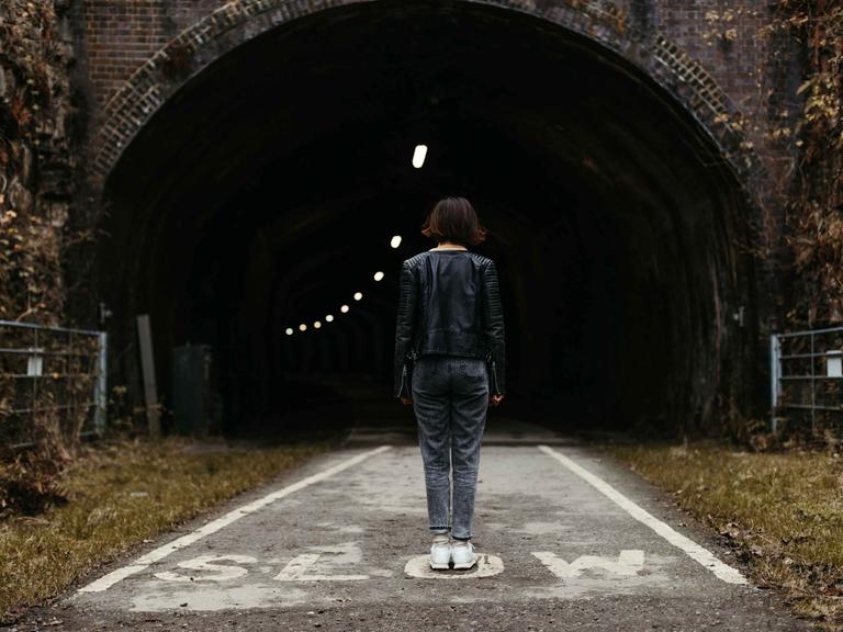 Rückansicht einer Frau, die mitten auf der Straße vor einem Tunnel steht. Rückansicht einer Frau, die mitten auf der Straße vor einem Tunnel steht.