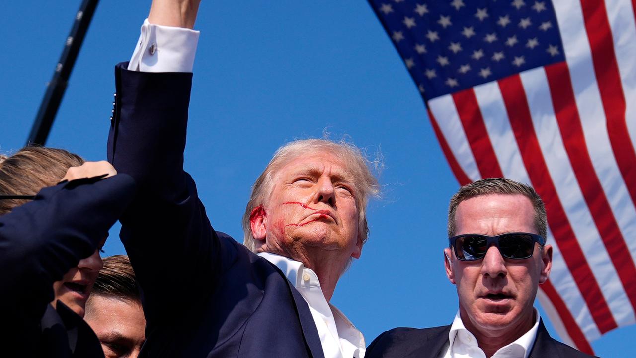Ex-US-Präsident Donald Trump reckt die Faust in den Himmel. An seinem rechten Ohr ist Blut zu sehen. Im Hintergrund: Die US-Flagge