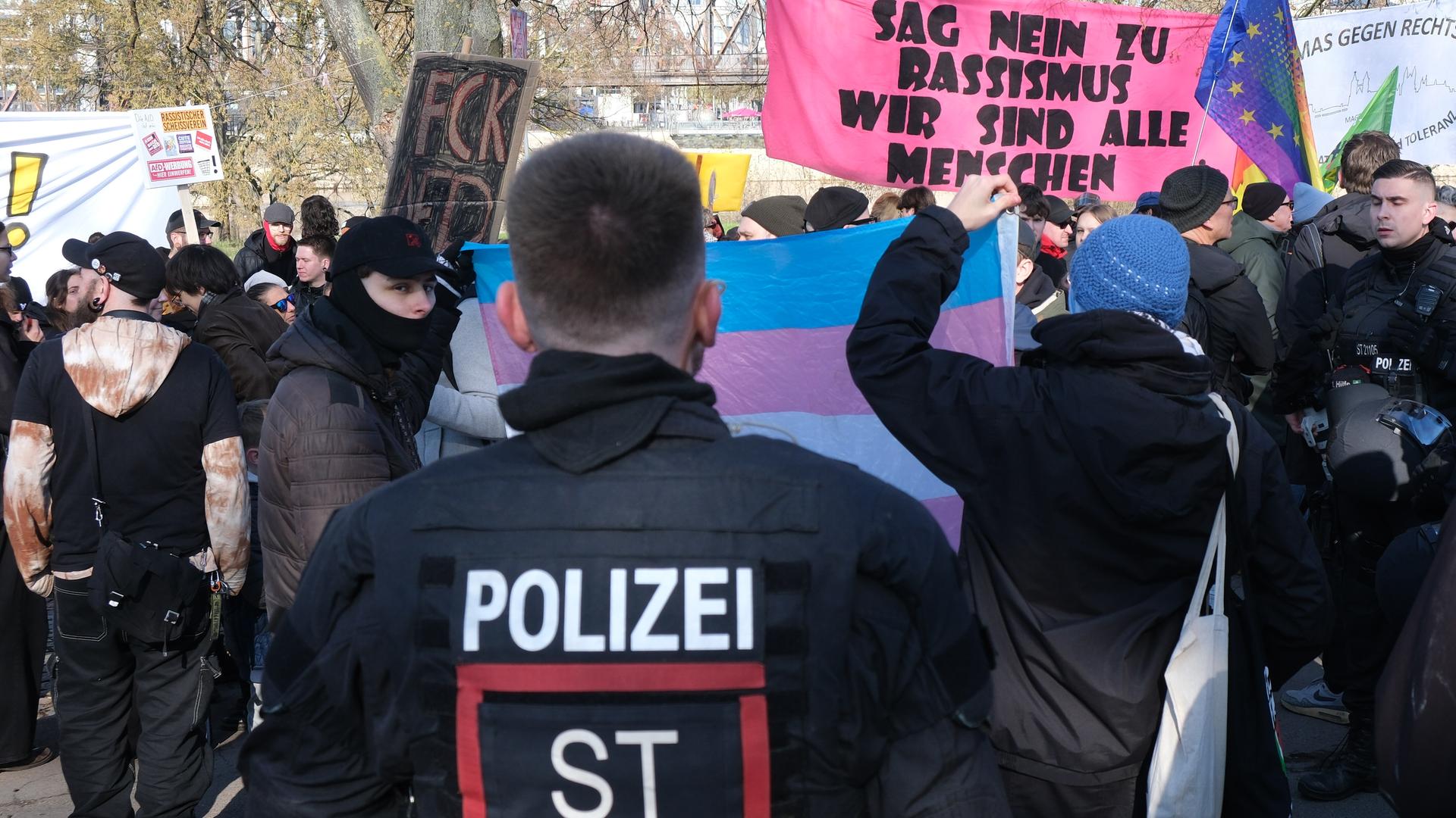 Im Hintergrund Demonstranten, die Plakate und Spruchbänder hochhalten, im Vordergrund ein Polizist. Im Hintergrund Demonstranten, die Plakate und Spruchbänder hochhalten, im Vordergrund ein Polizist.