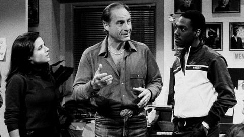 Ein Schwarz-Weiß-Foto zeigt die US-Komiker Julia Louis Dreyfus, Sid Caesar und Eddie Murphy (v. l.n.r.) in einer Ausgabe von „Saturday Night Live“ im Jahr 1983.