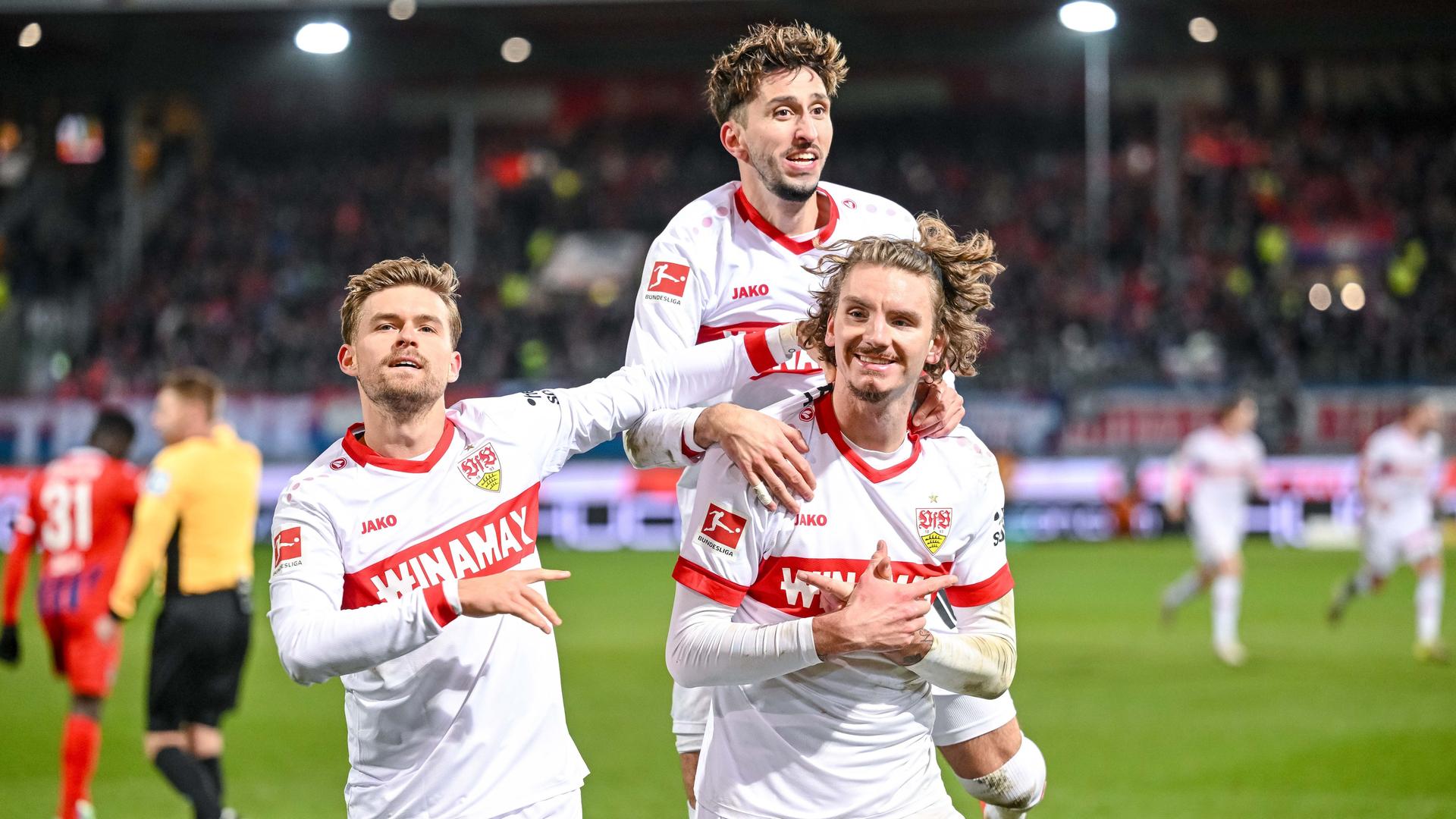 Die drei Spieler in den weiß-roten Trikots rennen jubelnd auf die Kamera zu. Im Hintergrund unscharf eine vollbesetzte Tribüne.
