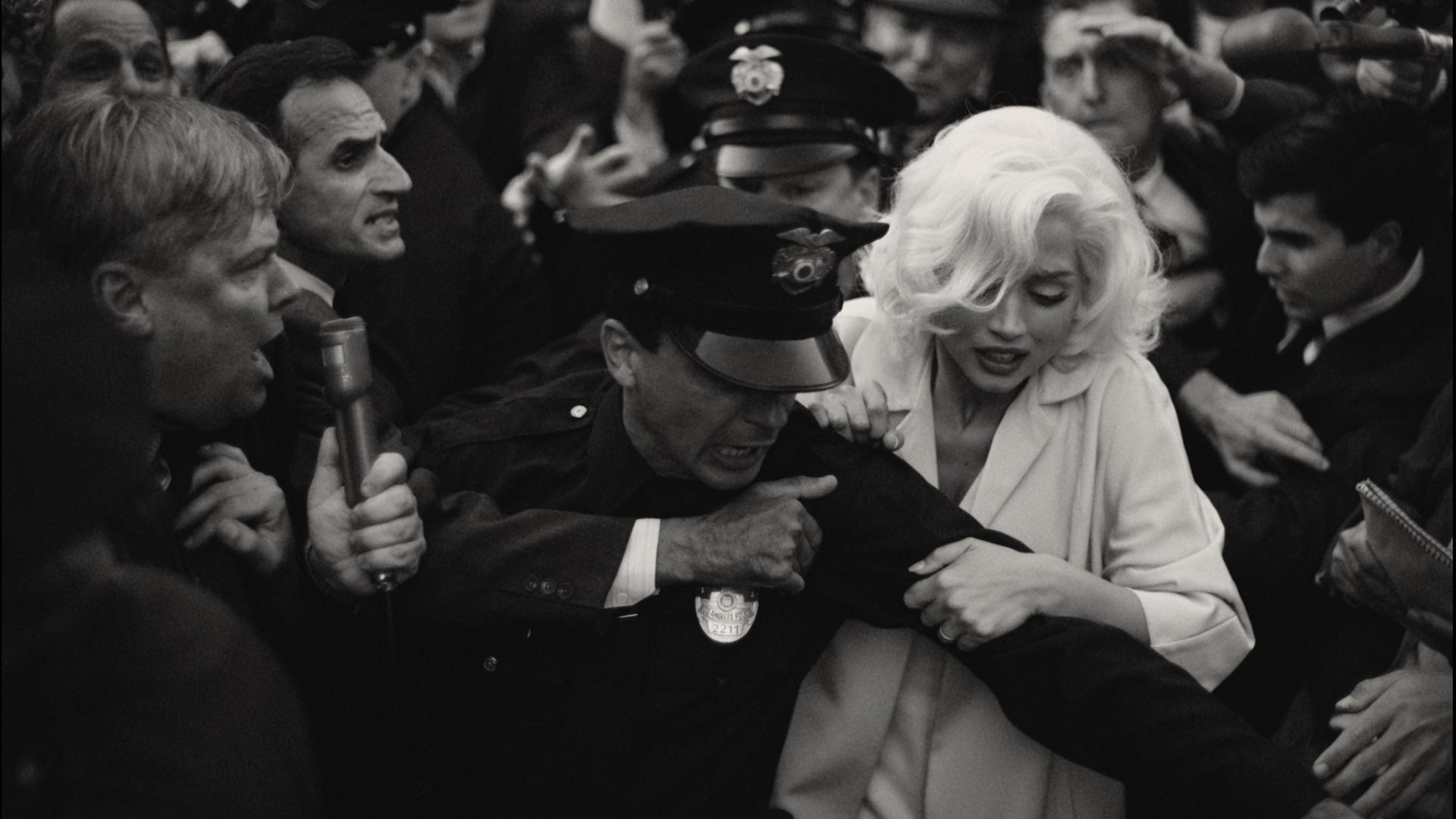 Die Filmszene in Schwarz-Weiß zeigt, wie Marilyn Monroe von einem Polizisten abgeführt wird.