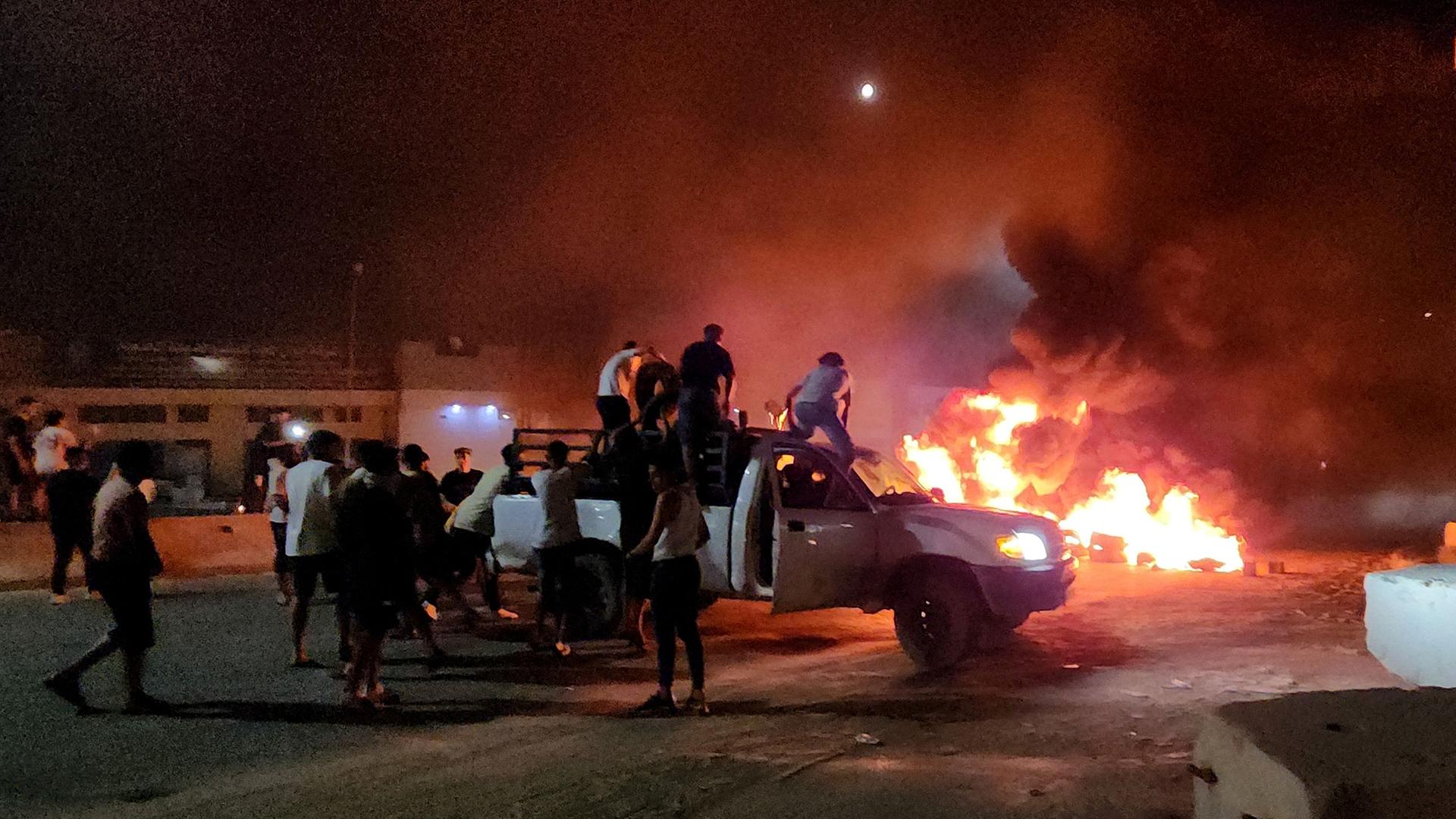 Libyen, Tripolis: Auf und neben einem Pickup sind Menschen, ein Auto brennt lichterloh.