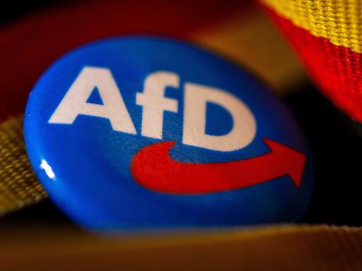 Symbolfoto AfD:Ein Ansteckpin mit dem Parteilogo der AfD (Alternative fuer Deutschland) liegt mit einer Deutschland-Banderole auf einem Tisch.