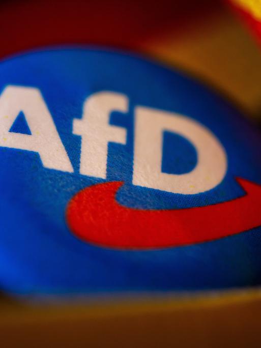 Symbolfoto AfD:Ein Ansteckpin mit dem Parteilogo der AfD (Alternative fuer Deutschland) liegt mit einer Deutschland-Banderole auf einem Tisch.