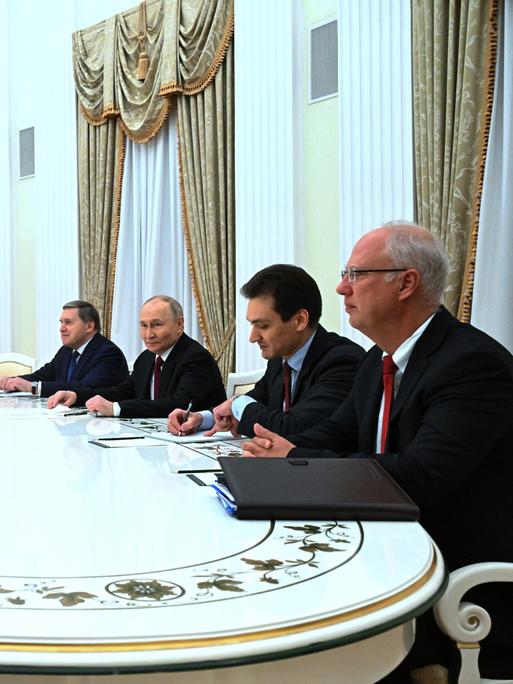 An einem großen weißen Tisch sitzen u.a. Russlands Präsident Wladimir Putin und die US-Sondergesandten Steve Witkoff und Jared Kushner