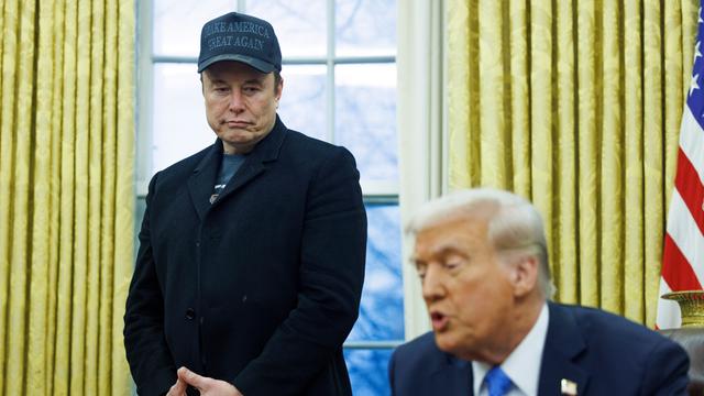 Elon Musk steht im Weißen Haus und blickt herab auf Donald Trump, der am Schreib-Tisch sitzt