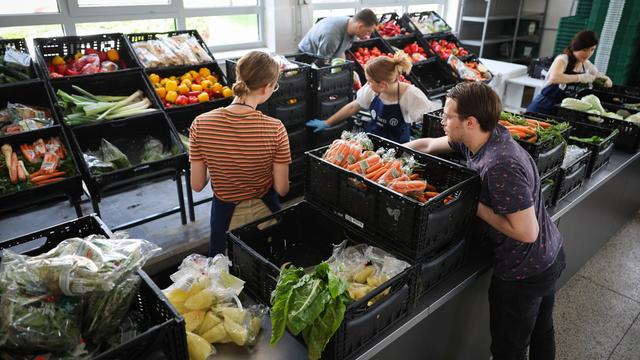 Ehren-amtliche Helfer und Helferinnen und sortieren Kisten mit Lebens-Mitteln in einem Raum der Tafel.  