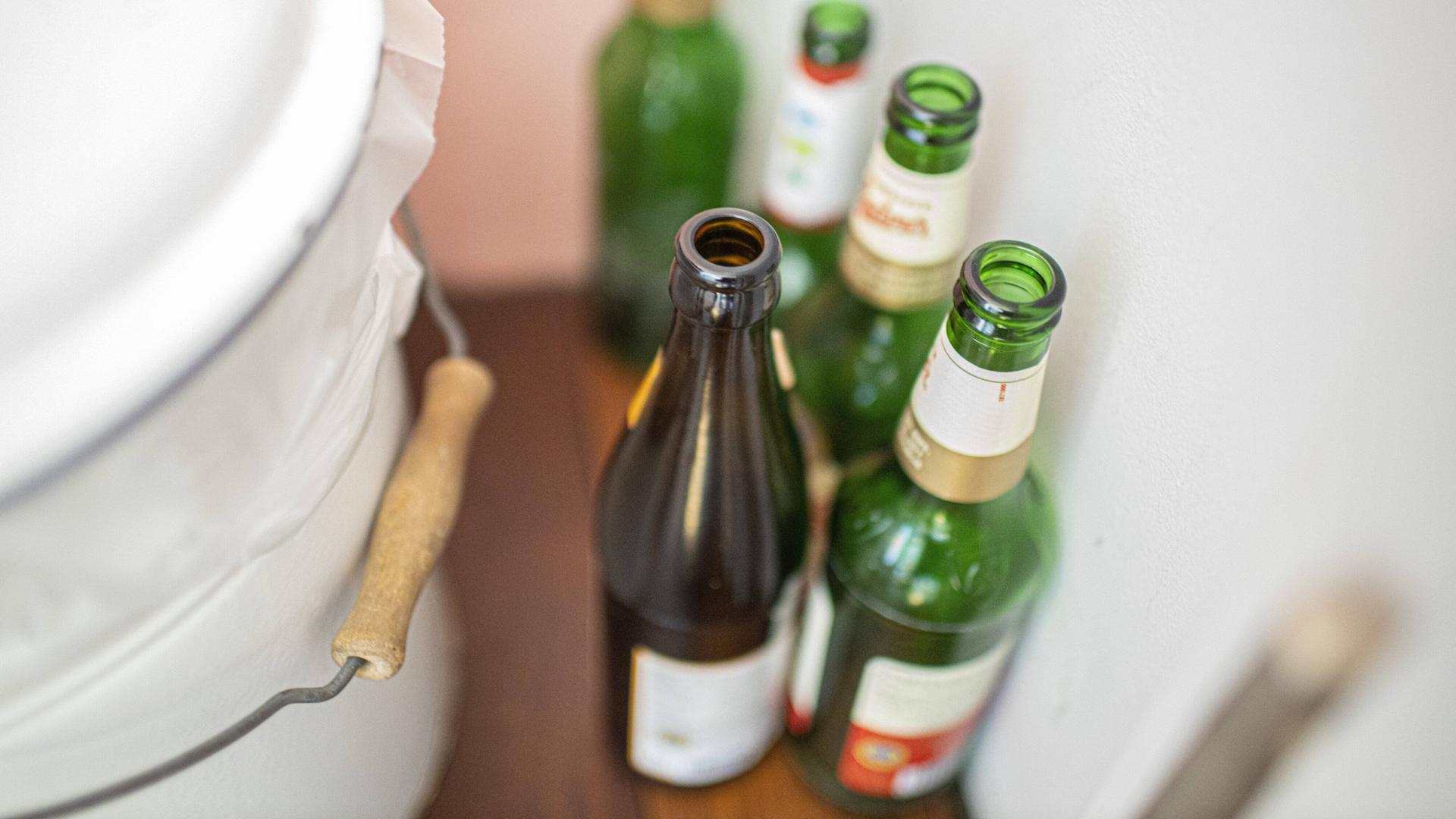 Leere Bierflaschen stehen neben einem Mülleimer in einer Wohnung.