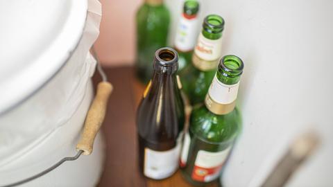 Leere Bierflaschen stehen neben einem Mülleimer in einer Wohnung.
