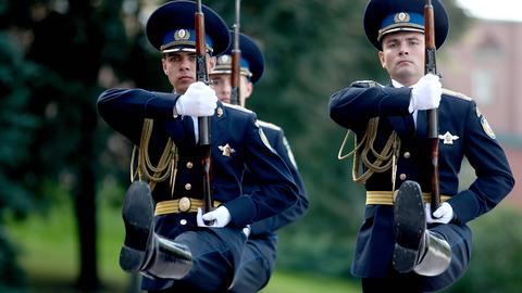 Russische Soldaten in blauer Uniform marschieren im Stechschritt und mit präsentiertem Gewehr.