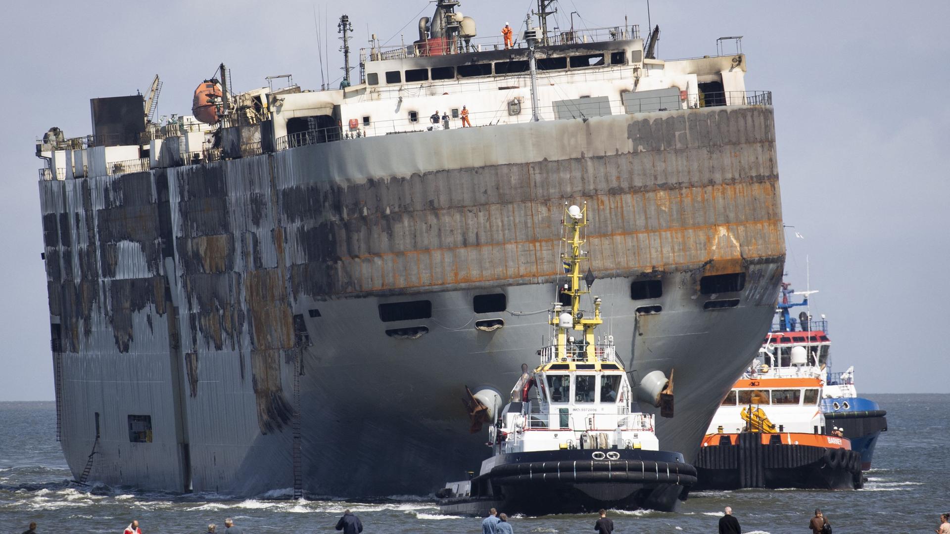 Menschen schauen zu, wie die "Fremantle Highway" von zwei Schleppern in den Hafen gezogen wird. Menschen schauen zu, wie die "Fremantle Highway" von zwei Schleppern in den Hafen gezogen wird.