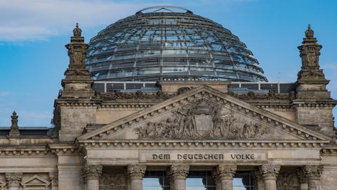 Der Reichstag in Berlin mit dem Schriftzug: "Dem Deutschen Volke". Im Hintergrund: Ein blauer Himmel. 