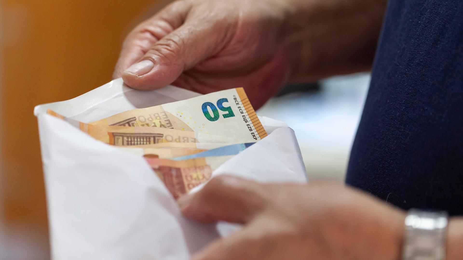 Euroscheine werden von einer Männerhand in einen Briefumschlag gesteckt.