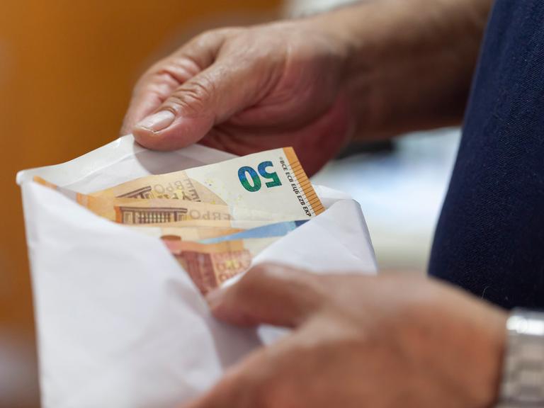 Euroscheine werden von einer Männerhand in einen Briefumschlag gesteckt.