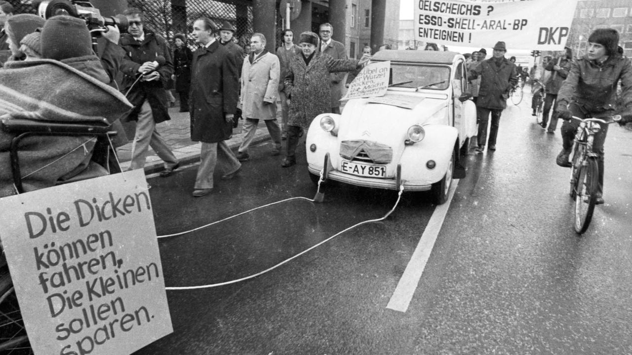 Autokorso der DKP am 24.11.1973 in Essen gegen die Fahrverbote an den autolosen Sonntagen . Die Fahrzeuge wurden jedoch von Menschen und Pferden gezogen und geschoben. Auf einem Schild ist zu lesen: "Die Dicken können fahren, die Kleinen sollen sparen."