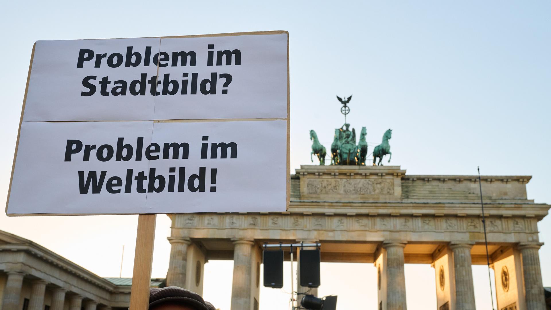 "Problem im Stadtbild? - Problem im Weltbild" steht auf einem Plakat, das ein Demonstrant vor dem Brandenburger Tor hält. 
