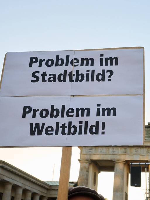 "Problem im Stadtbild? - Problem im Weltbild" steht auf einem Plakat, das ein Demonstrant vor dem Brandenburger Tor hält. 