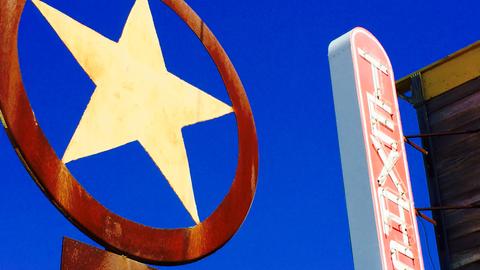 Ein rostiger Texas Lone Star und ein Texas-Schriftzug in Leuchtschrift vor einem intensivblauen Himmel.