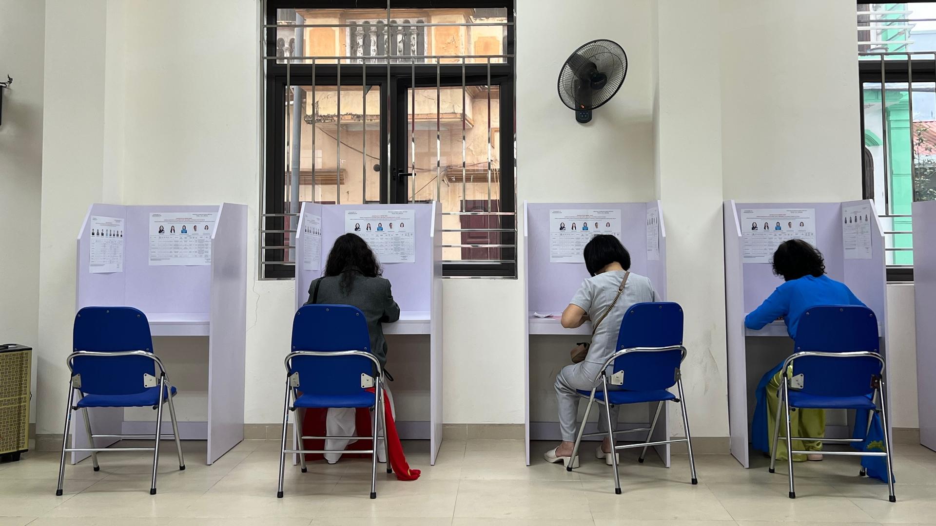 Menschen sitzen in Wahlkabinen, die vor einer Wand aufgereiht sind. Menschen sitzen in Wahlkabinen, die vor einer Wand aufgereiht sind.