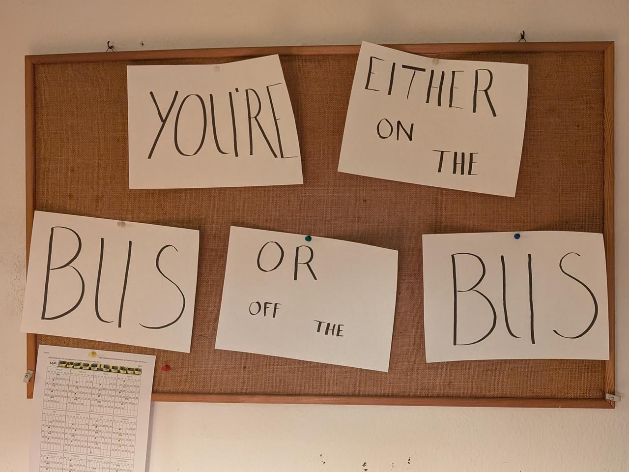 Eine Pinnwand in der Küche des Hauses, an der mehrere Zettel hängen auf denen steht „You’re either on the bus or off the bus“ Eine Pinnwand in der Küche des Hauses, an der mehrere Zettel hängen auf denen steht „You’re either on the bus or off the bus“