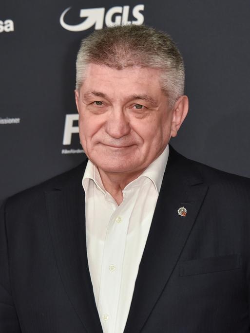 Der Filmemacher Alexander Sokurow steht vor einer Werbewand und guckt in die Kamera