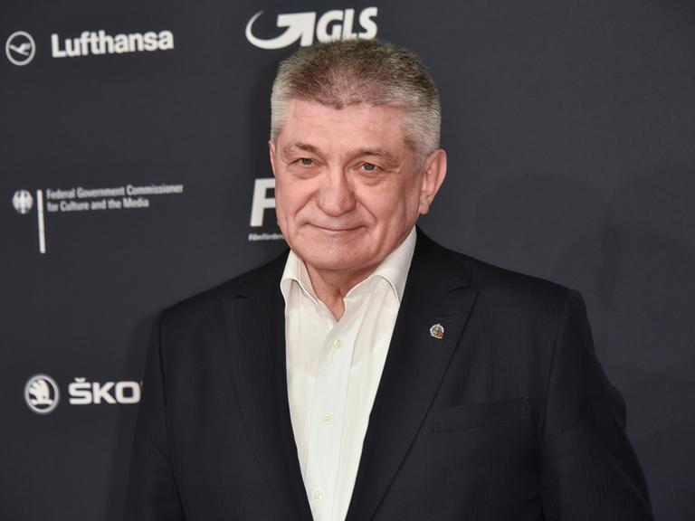 Der Filmemacher Alexander Sokurow steht vor einer Werbewand und guckt in die Kamera