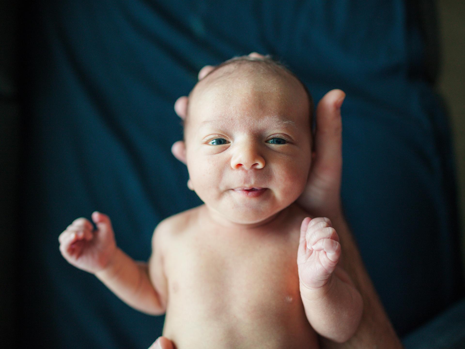Ein neugeborenes Baby, der kleine Kopf liegt in einer grossen Hand.