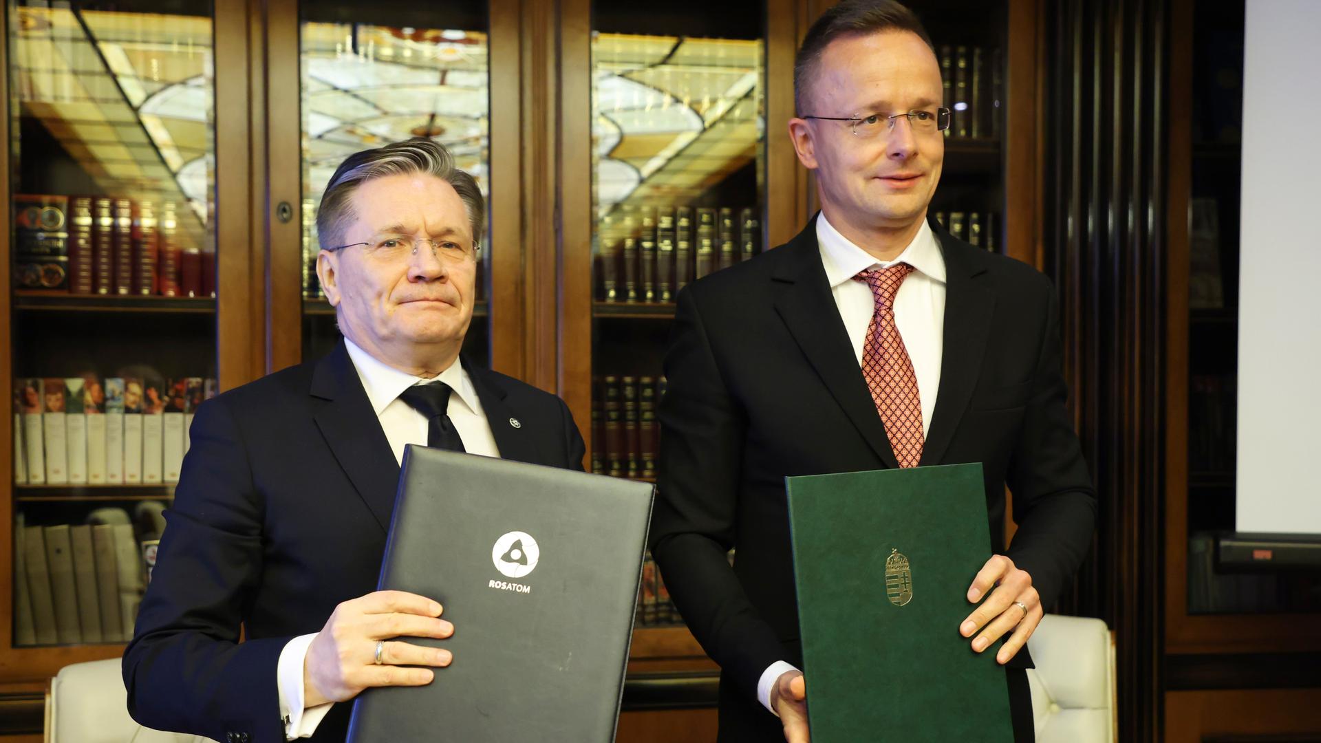 Der ungarische Außenminister Peter Szijjarto steht neben dem Direktor des Communications Department of Rosatom, Alexey Likhachev. Beide halten ein Dokument in den Händen. Der ungarische Außenminister Peter Szijjarto steht neben dem Direktor des Communications Department of Rosatom, Alexey Likhachev. Beide halten ein Dokument in den Händen.