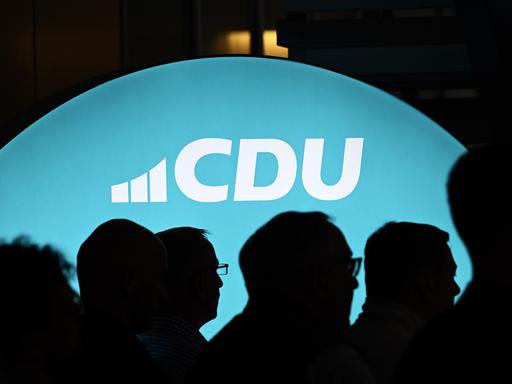 Ein beleuchtetes Banner mit dem Schriftzug "CDU" ist zu sehen, davor sieht man im Schatten die Köpfe mehrerer Menschen. Ein beleuchtetes Banner mit dem Schriftzug "CDU" ist zu sehen, davor sieht man im Schatten die Köpfe mehrerer Menschen.