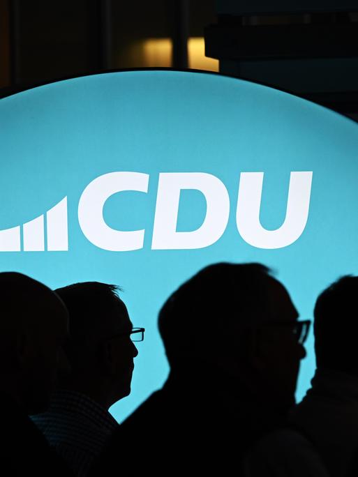 Ein beleuchtetes Banner mit dem Schriftzug "CDU" ist zu sehen, davor sieht man im Schatten die Köpfe mehrerer Menschen. Ein beleuchtetes Banner mit dem Schriftzug "CDU" ist zu sehen, davor sieht man im Schatten die Köpfe mehrerer Menschen.