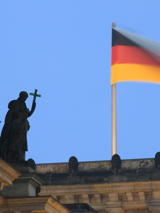 Auf dem Reichstagsgebäude weht eine Deutsche Fahne und eine Statue aus Stein hält ein Kreuz als Symbol für die christliche Kirche, Berlin, Deutschland, Europa