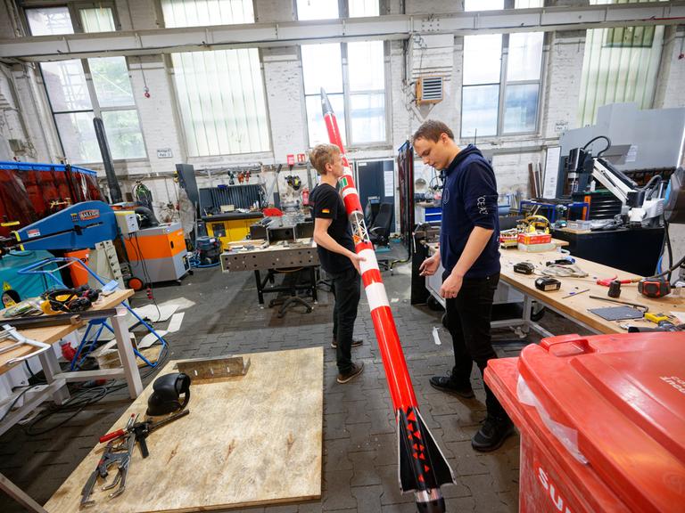 Die Studenten Florian Schuler (l) und Johann Schepke vom Space Team Aachen stehen mit ihrer Rakete in der Werkstatt. Der Flugkörper soll mit zweifacher Schallgeschwindigkeit von einem Schiff von der Nordsee aus starten.