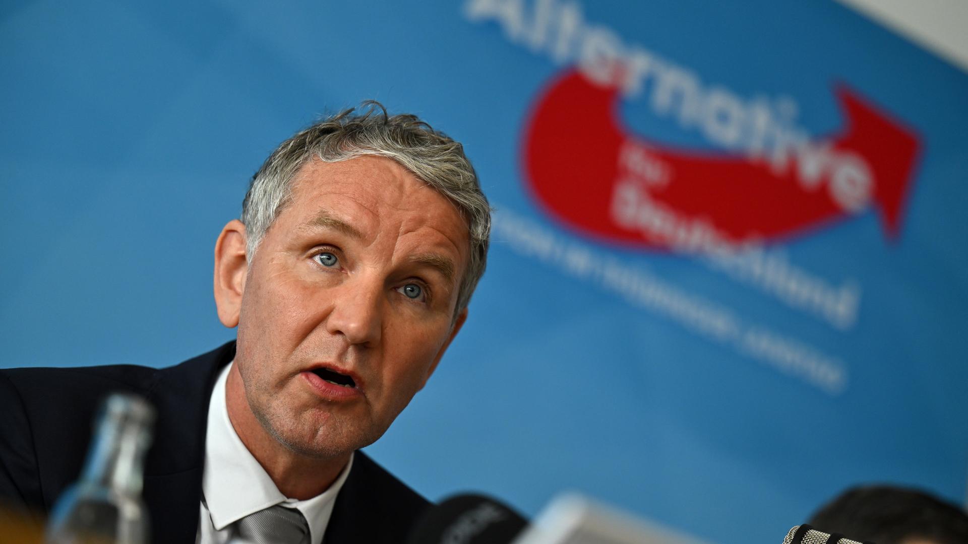 Björn Höcke sitzt vor einer blauen Wand mit dem Logo seiner Partei.