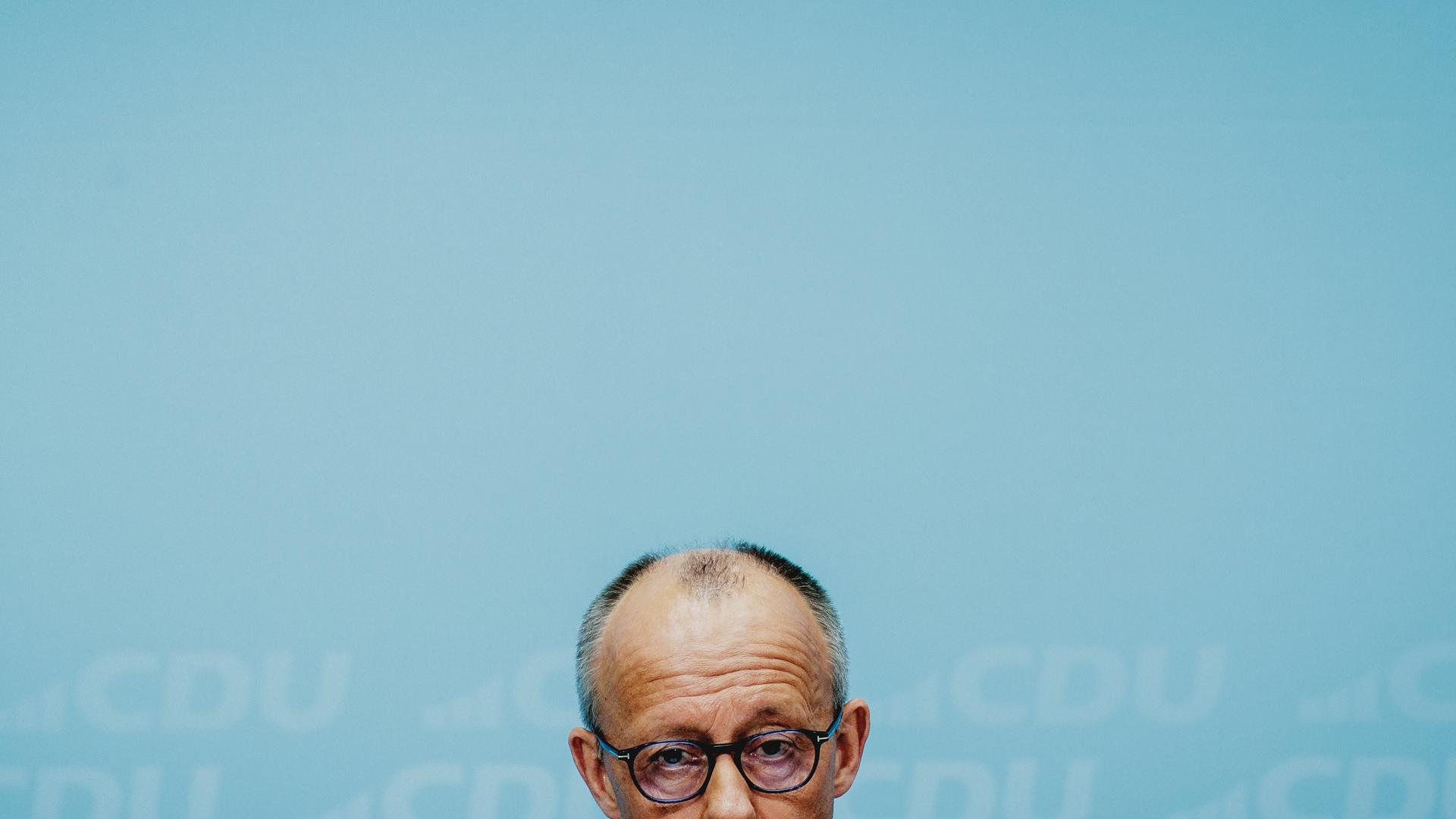 Die obere Hälfte von Friedrich Merz' Kopf am untern Bildrand vor dem grünblauen Hintergrund einer Wand