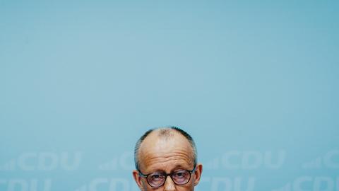Die obere Hälfte von Friedrich Merz' Kopf am untern Bildrand vor dem grünblauen Hintergrund einer Wand