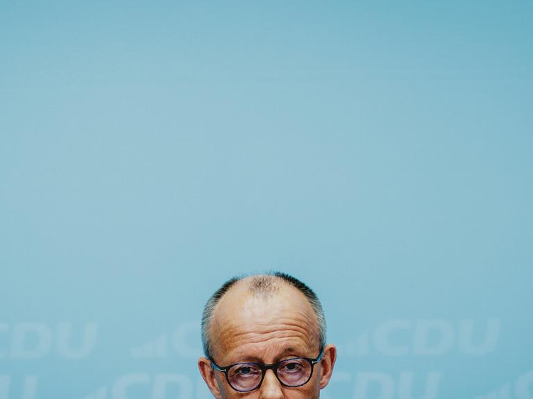 Die obere Hälfte von Friedrich Merz' Kopf am untern Bildrand vor dem grünblauen Hintergrund einer Wand Die obere Hälfte von Friedrich Merz' Kopf am untern Bildrand vor dem grünblauen Hintergrund einer Wand