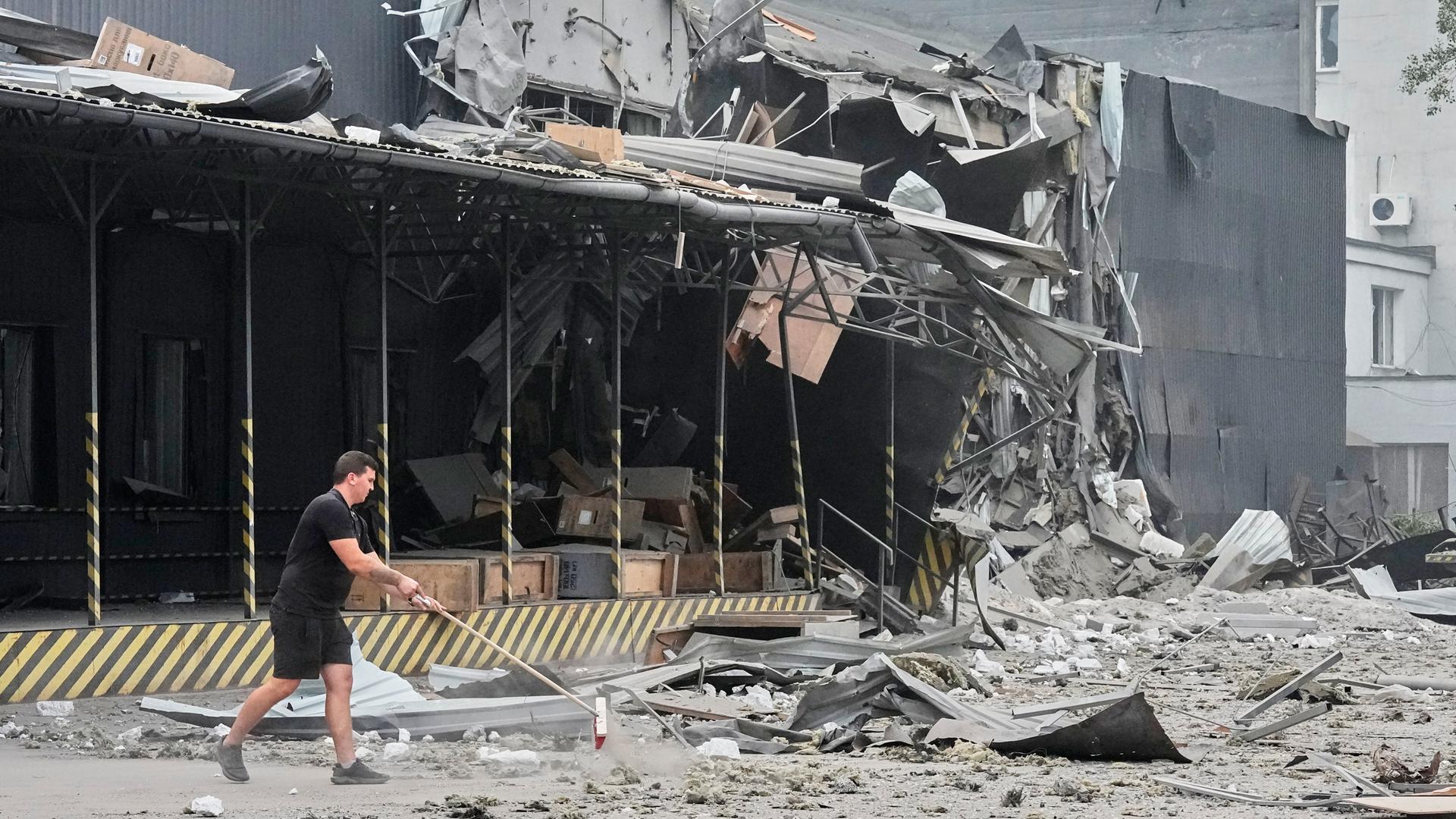 Ein Man kehrt die Straße vor einer völlig zerstörten Lagerhalle. Ein Man kehrt die Straße vor einer völlig zerstörten Lagerhalle.