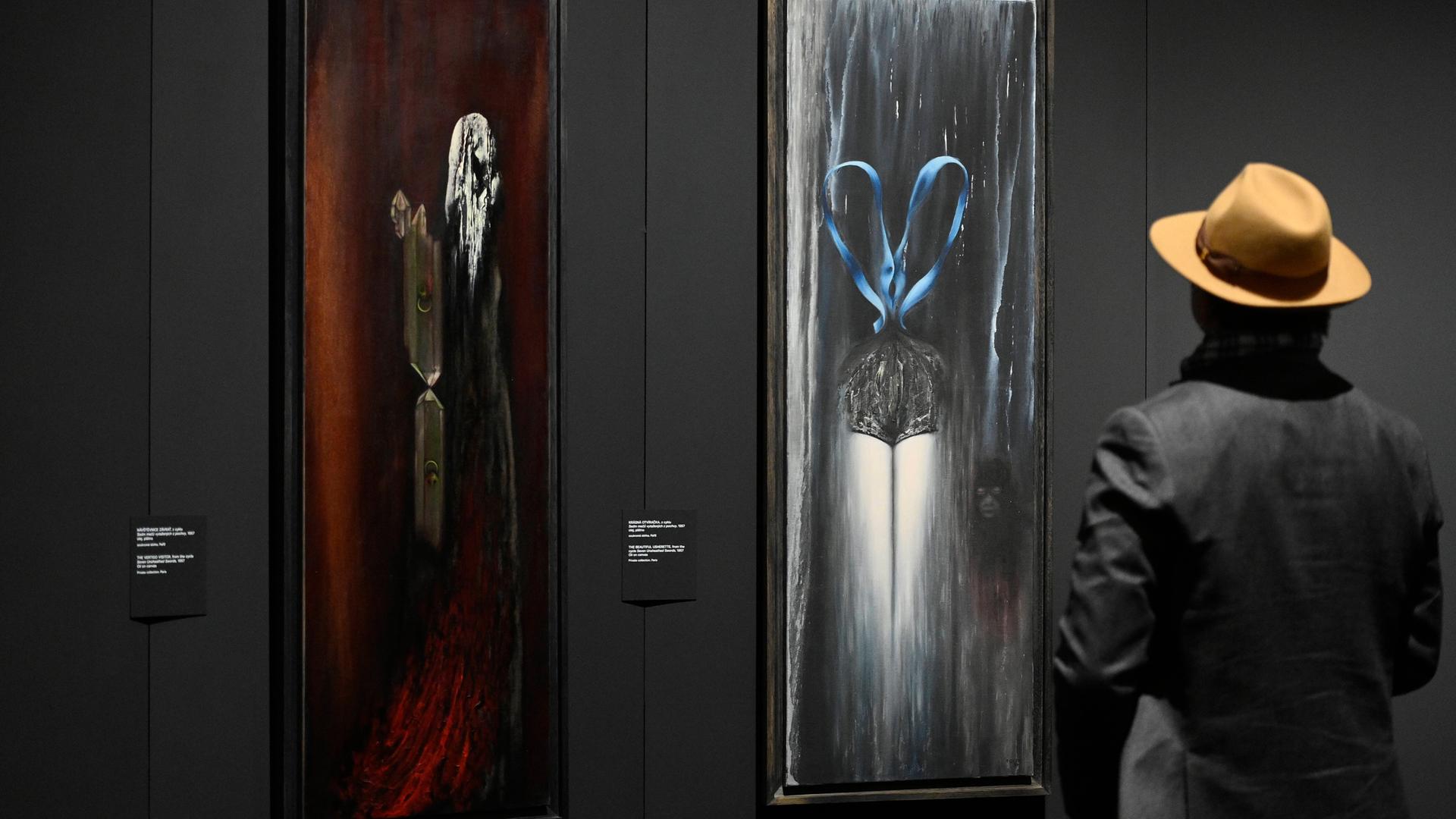 Toyen Gemälde in der "Dreaming Rebel" Ausstellung in der Nationalgalerie in Prag. Eine Person mit Hut betrachtet die Bilder.