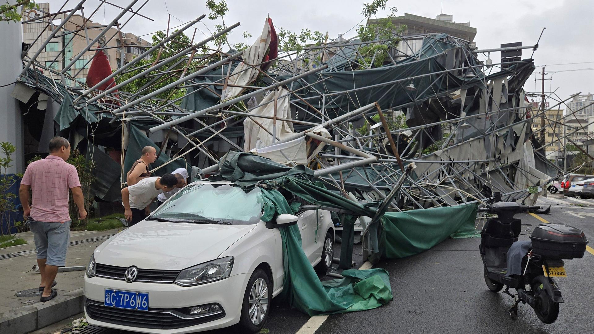 China, Wenzhou: Menschen blicken in der ostchinesischen Provinz Zhejiang in das Innere eines Autos, das von einem umgestürzten Gerüst eingeklemmt wurde, nachdem der Taifun "Dolphin" die Region heimgesucht hatte. China, Wenzhou: Menschen blicken in der ostchinesischen Provinz Zhejiang in das Innere eines Autos, das von einem umgestürzten Gerüst eingeklemmt wurde, nachdem der Taifun "Dolphin" die Region heimgesucht hatte.