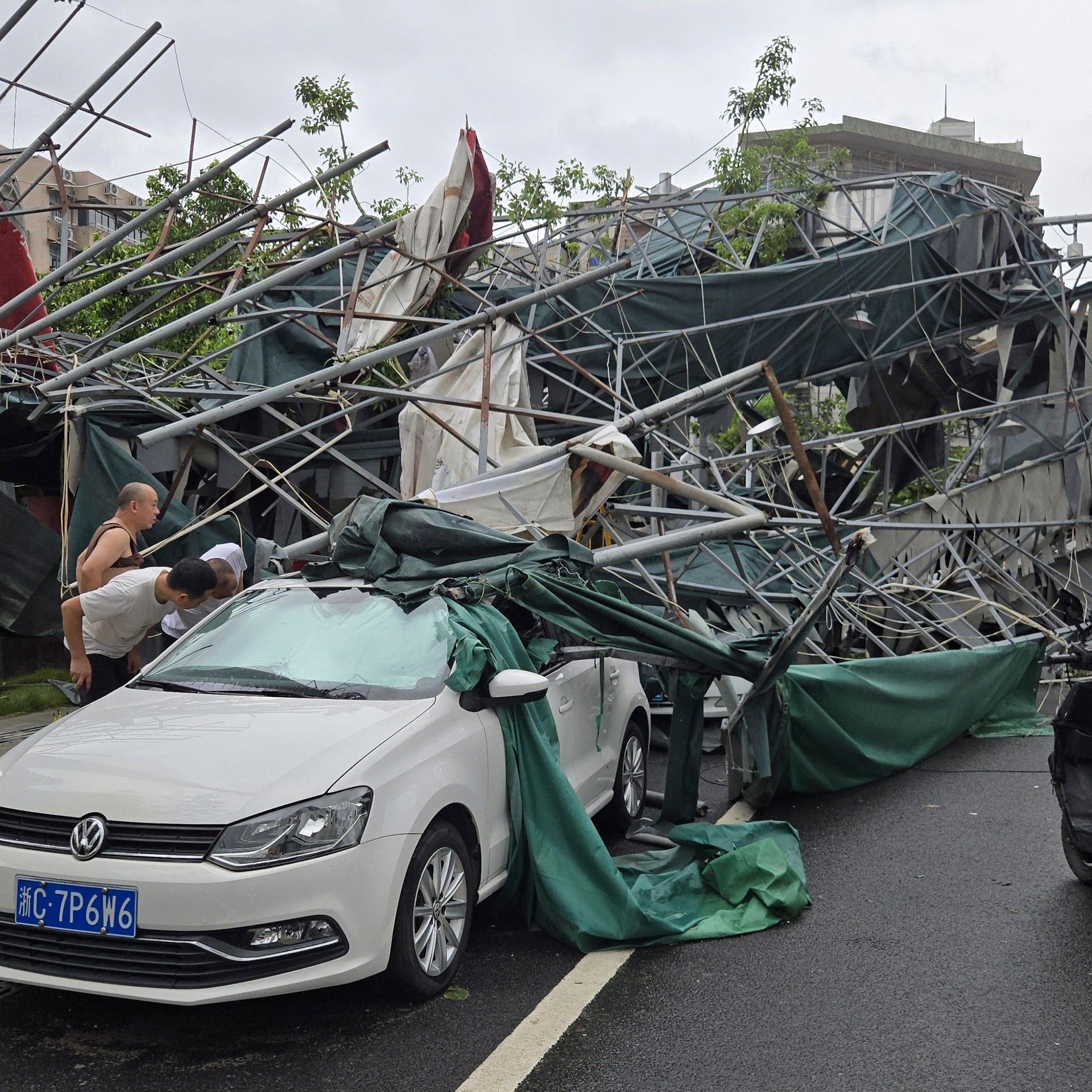 China, Wenzhou: Menschen blicken in der ostchinesischen Provinz Zhejiang in das Innere eines Autos, das von einem umgestürzten Gerüst eingeklemmt wurde, nachdem der Taifun "Dolphin" die Region heimgesucht hatte. 