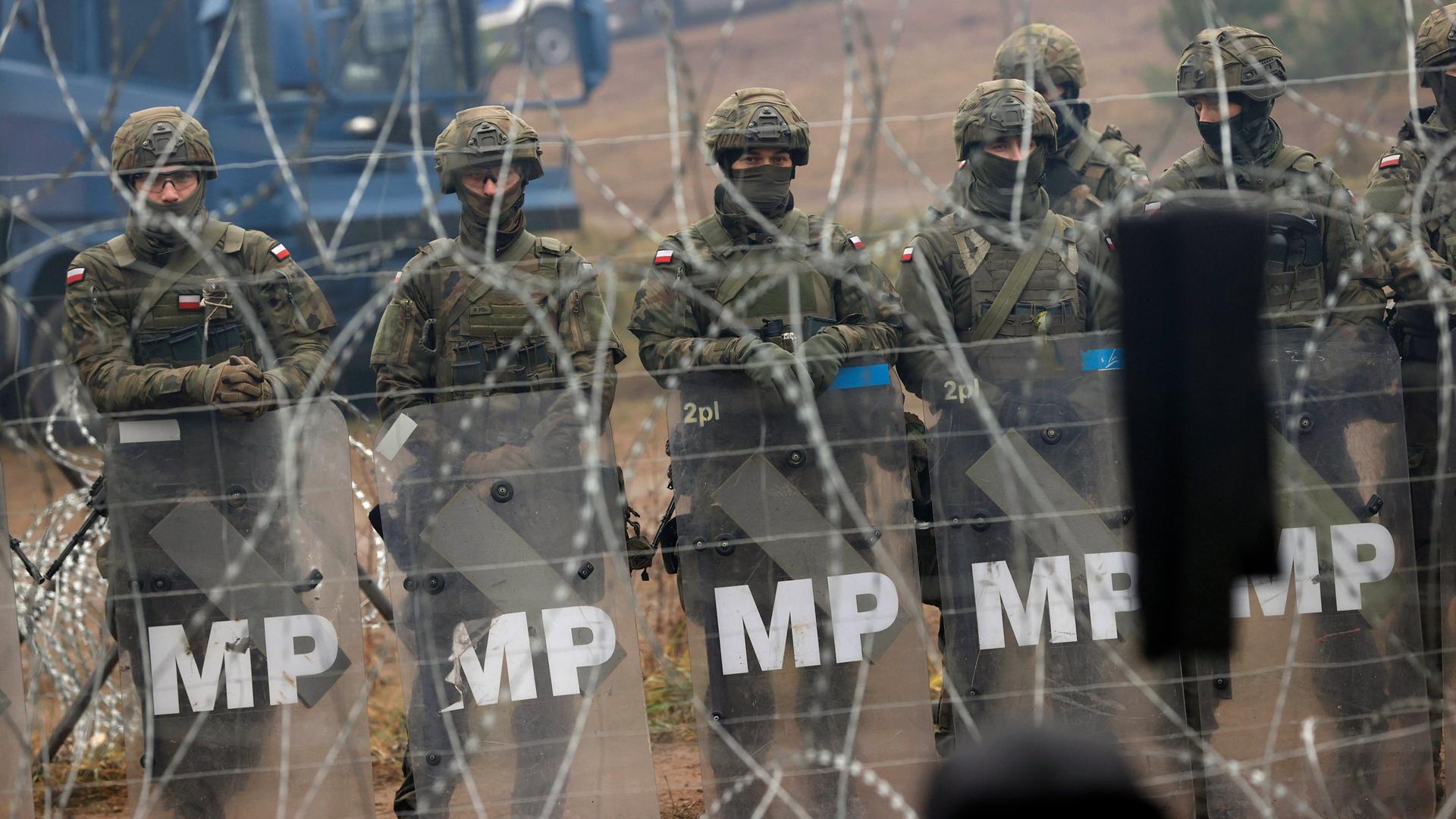 Polnische Sicherheitskräfte in schwerer Montur an der Grenze zu Belarus, hinter einem Stacheldraht. 