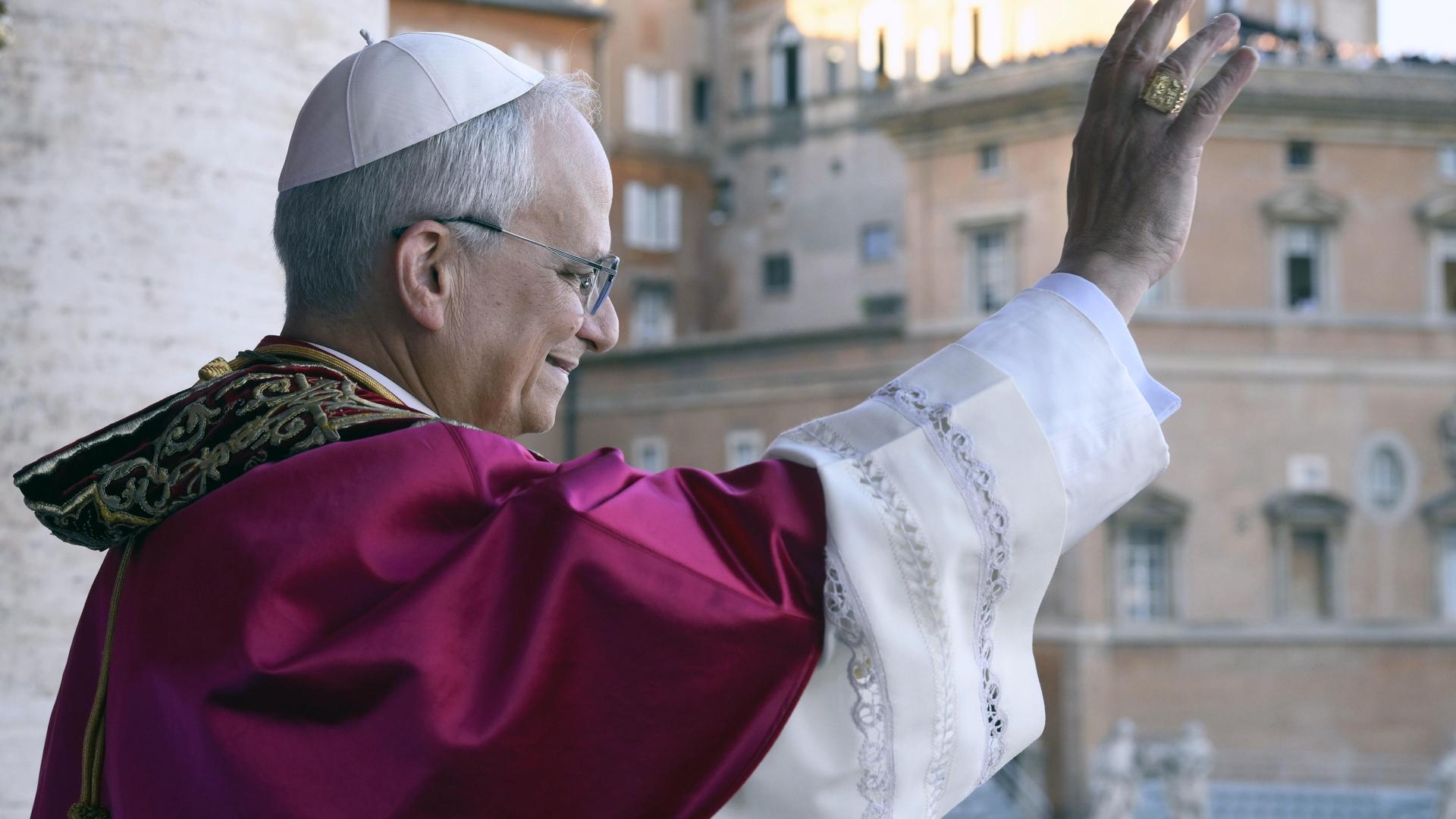 Papst Leo XIV. winkt den Gläubigen von seiner Mittelloggia des Petersdoms aus zu. Das Foto zeigt ihn im Profil und im leichten Gegenlicht.