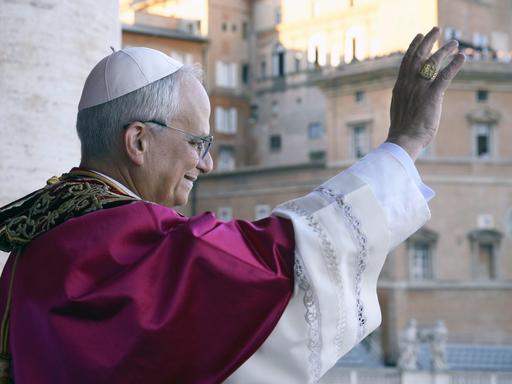 Papst Leo XIV. winkt den Gläubigen von seiner Mittelloggia des Petersdoms aus zu. Das Foto zeigt ihn im Profil und im leichten Gegenlicht.