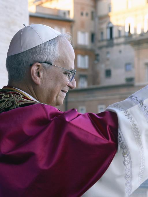 Papst Leo XIV. winkt den Gläubigen von seiner Mittelloggia des Petersdoms aus zu. Das Foto zeigt ihn im Profil und im leichten Gegenlicht.