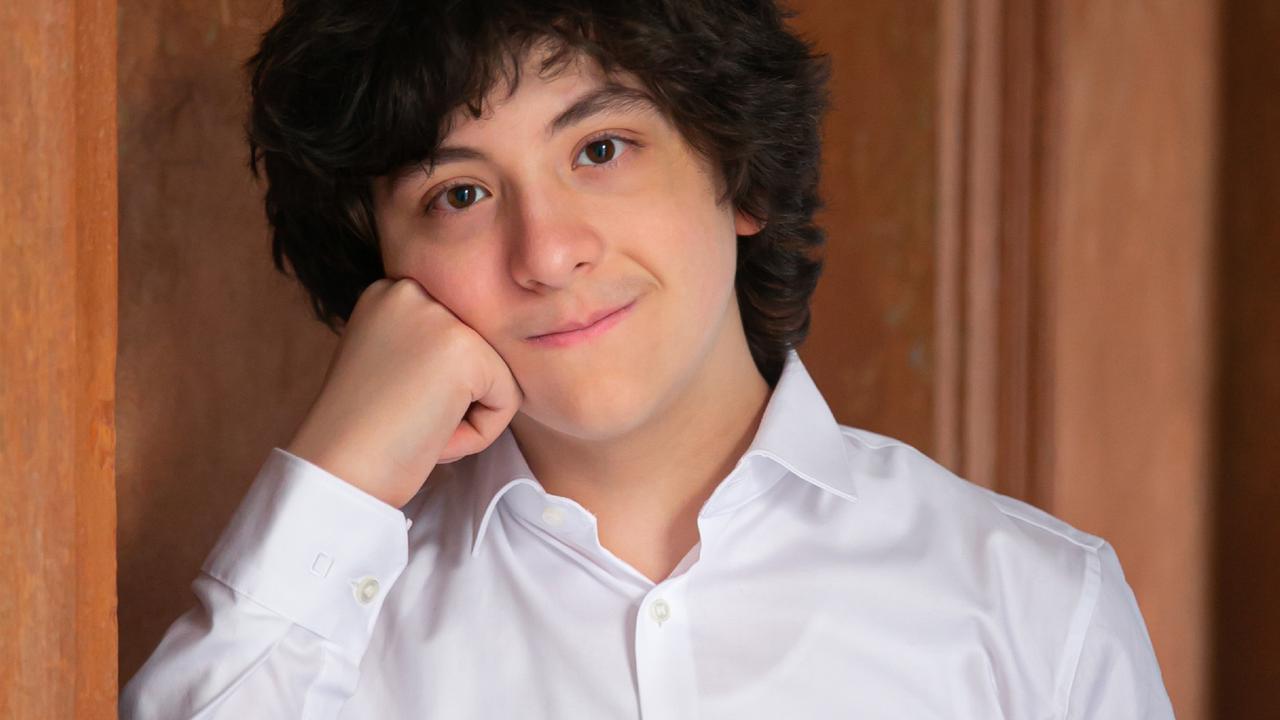 Ein junger Mann mit weißem Hemd, dunklen Locken und offenen Augen schaut in die Kamera. Ein junger Mann mit weißem Hemd, dunklen Locken und offenen Augen schaut in die Kamera.