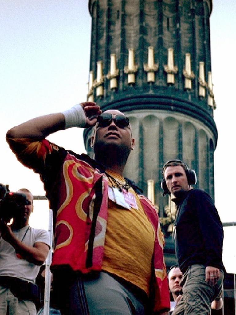 Still aus dem Film "be.Angeled", in dem Mark Spoon vor der Berliner Siegessäule steht. Er trägt ein buntes Hemd und Sonnenbrille. Fans jubeln ihm zu.