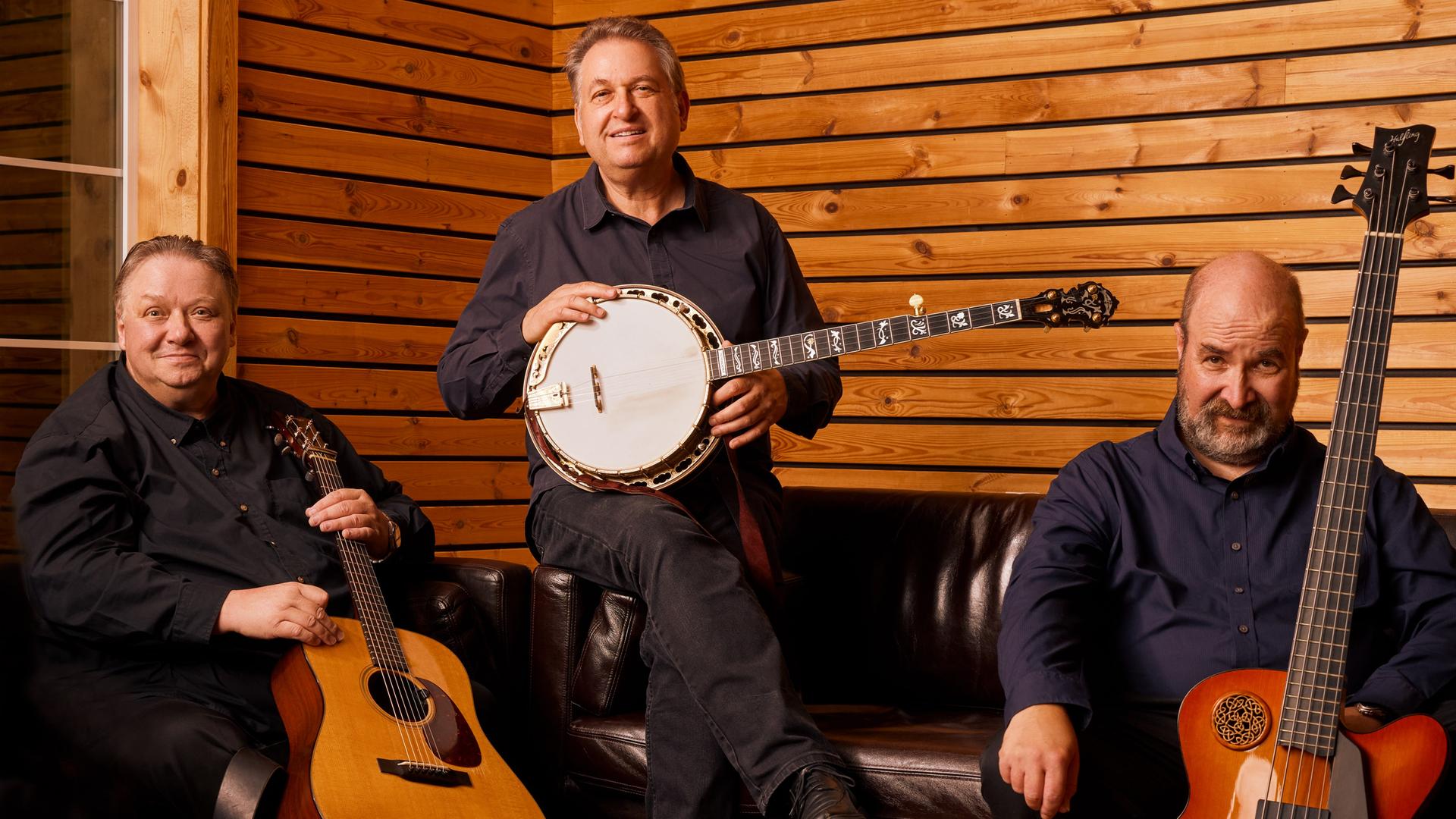 Drei Männer mit ihren Instrumenten sitzen in einem mit Holz vertäfelten Raum mit ihren Instrumenten.